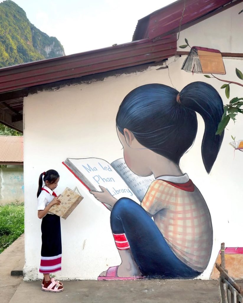 Child reading beside Seth Globepainter Tree of Books mural